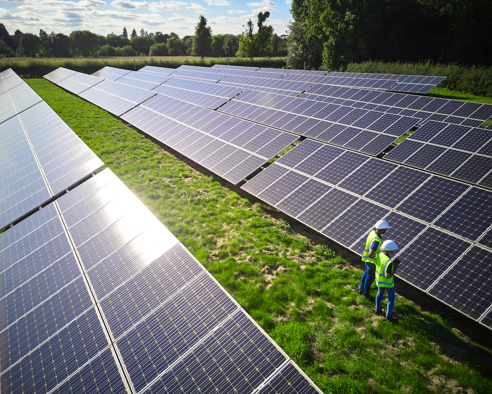Luftaufnahme mit einer Drohne von Ingenieuren, die Solarmodule auf einem Feld inspizieren, auf dem erneuerbare Energie erzeugt wird