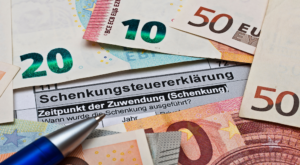 Euro-Geldscheine, ein Kugelschreiber und eine Schenkungsteuererklärung zum Thema Vermögen verschenken
