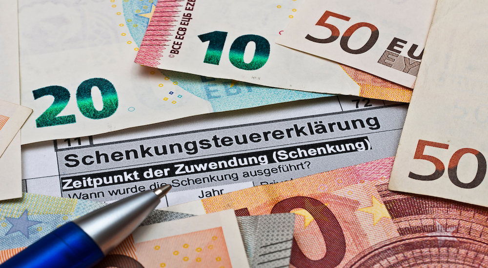Euro-Geldscheine, ein Kugelschreiber und eine Schenkungsteuererklärung zum Thema Vermögen verschenken